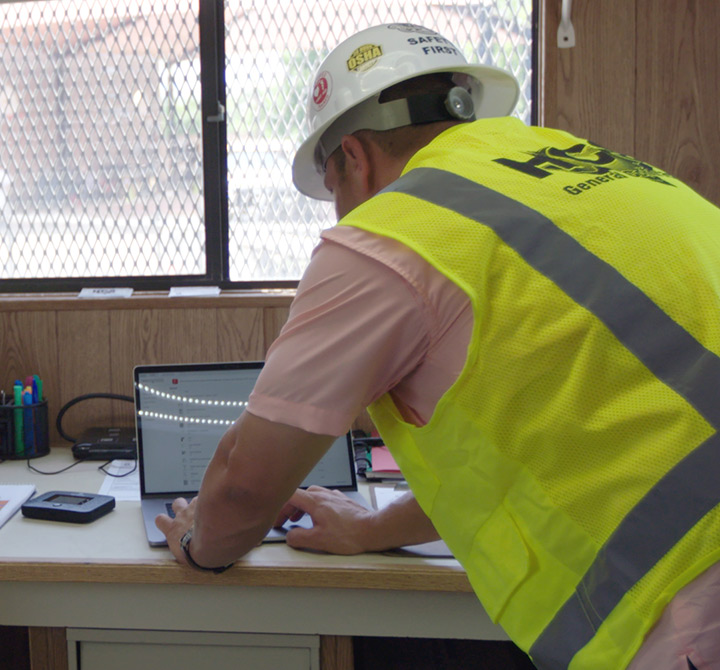 Construction man in hardhat and vest using a laptop.